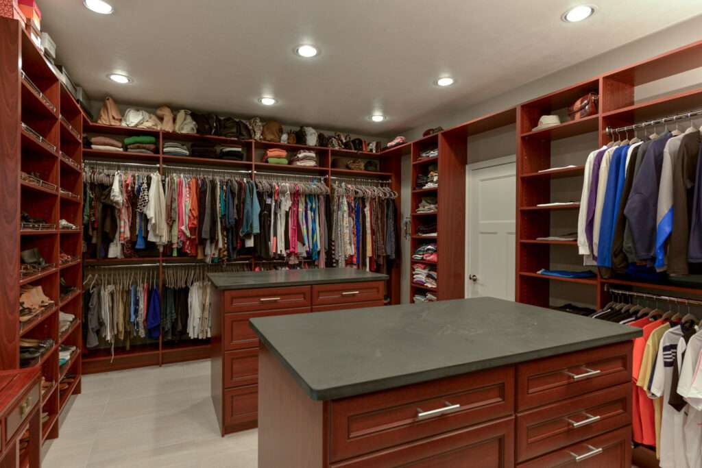 photo of a master closet filled with clothes and 2 islands that have drawers