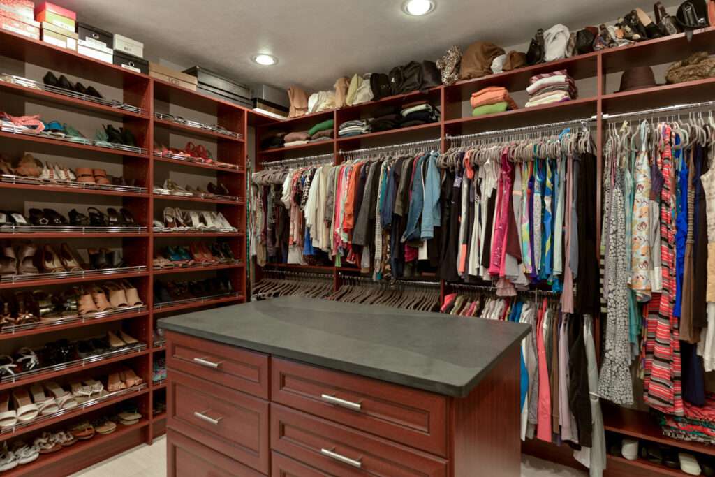 photo of a master closet filled with clothes and an island that has drawers