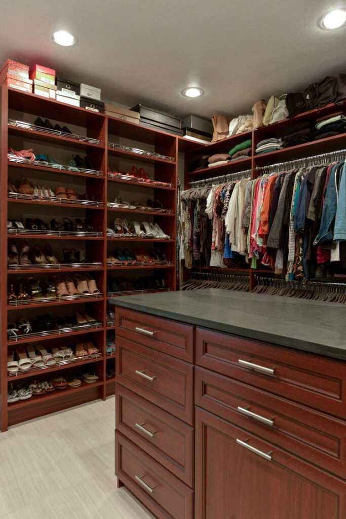 photo of a master closet filled with clothes and an island that has drawers