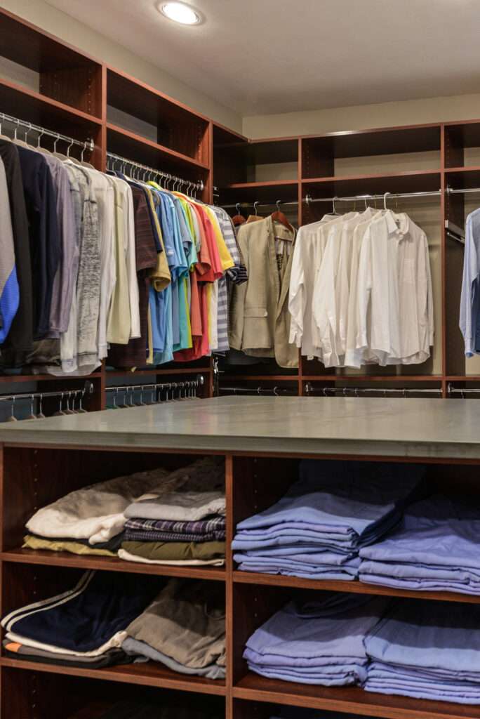 His Master Closet with Hanging Clothes and an island filled with folded shirts