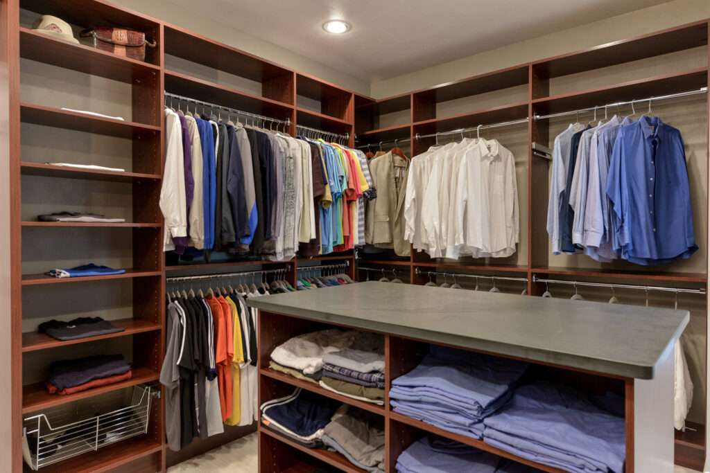 His Master Closet with Hanging Clothes and an island filled with folded shirts